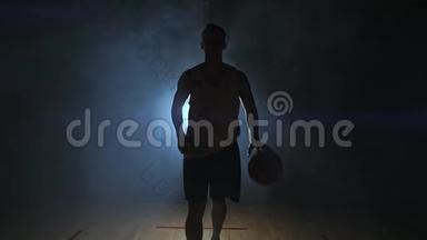 篮球运动员在一个黑暗的房间里径直走向摄像机，烟雾中有一个背光的背部看着摄像机。